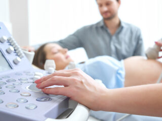 Selective focus on doctor hand operating ultrasound scanning machine pregnant couple on the background copyspace procedure treatment healthcare research medicine expecting childbirth parents.